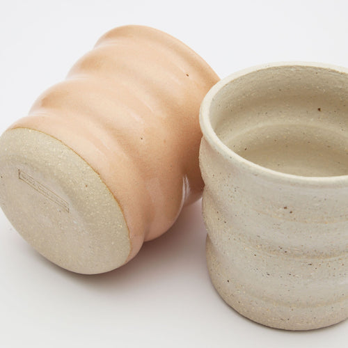 Two ceramic cups. One is glazed in a bright pink colour the other is a pebble stone.