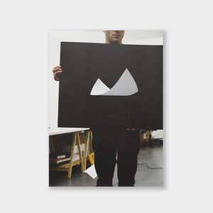 A limited edition artwork by Ryan Gander. In the photo, a person wearing black trousers holds a black canvas with a floating white piece of paper on it.