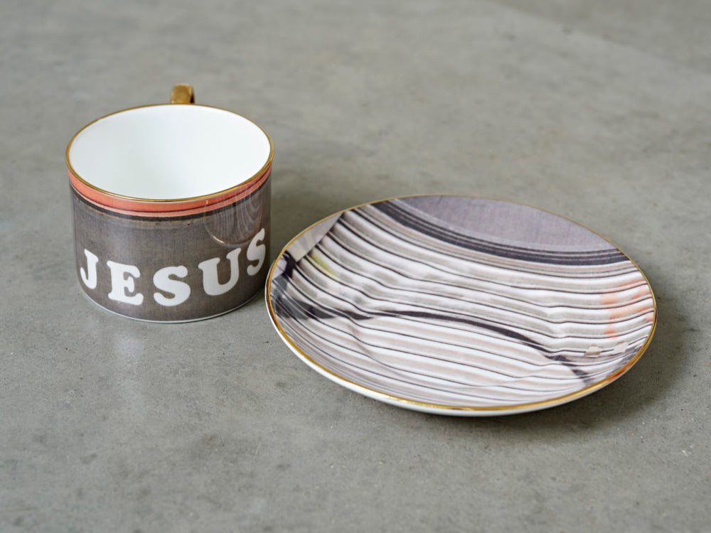 A china teacup and saucer by artist Rene Matic. The teacup has been printed with the word Jesus.