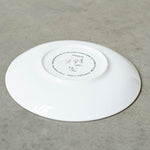 A white china saucer placed upside down on a grey surface.