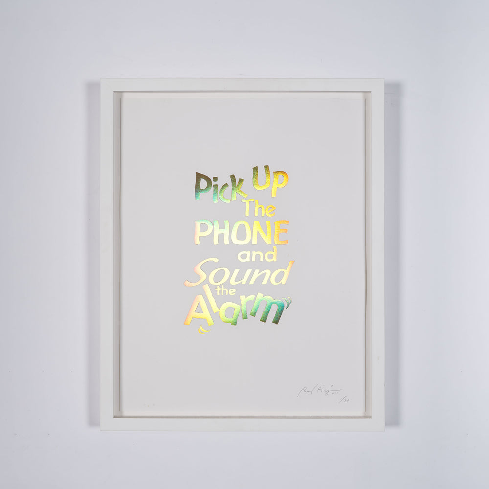 A framed print of a white page with metallic gold letters on it. This is a limited edition artwork by Rory Pilgrim. The text says Pick Up The Phone and Sound the alarm.