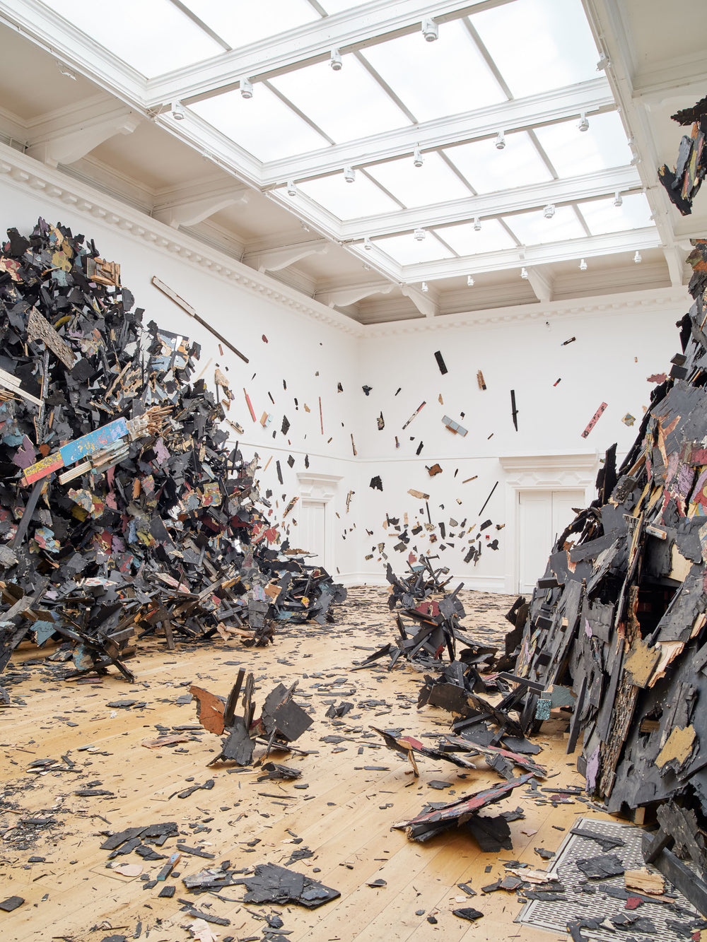 An installation photo of Leonardo Drew, Ubiquity II at the South London Gallery. The gallery has been taken over by an immersive installation made up of broken, black pieces of wood.