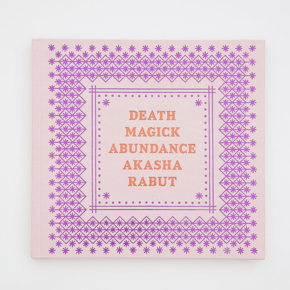 A square book with a purple pattern and orange writing. The book is titled Death Magick Abundance.