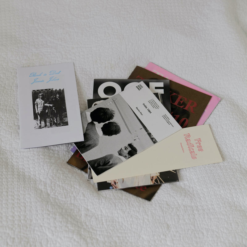 A pile of magazines and zines lie on a bed.