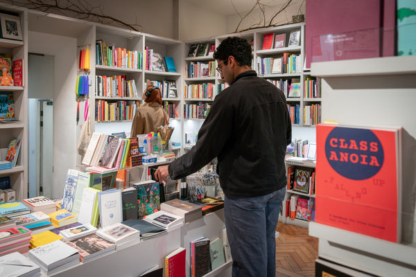 Person browsing books in a bookstore with shelves filled with books and a visible 'Class Anoia' book.