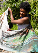 A woman in a sunlit garden dancing with a scarf