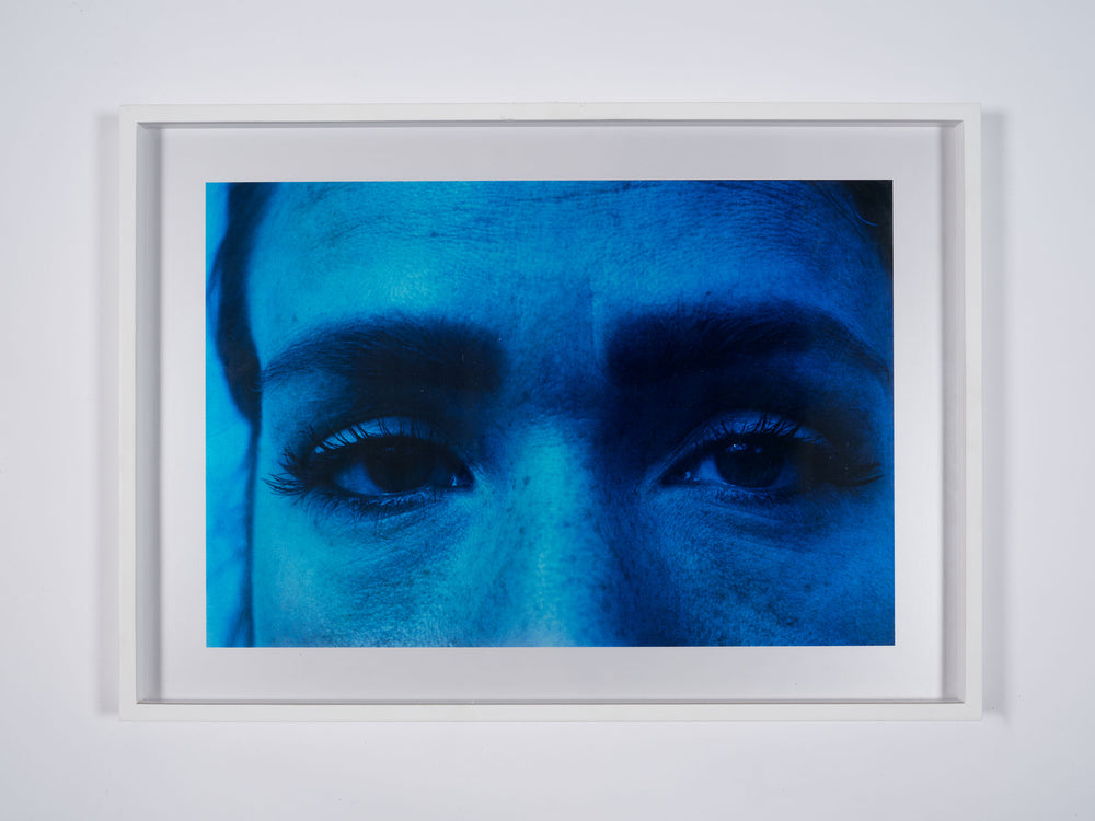 A framed print by artist Basim Magdy. A close up photograph of a woman's face, with a blue filter. 