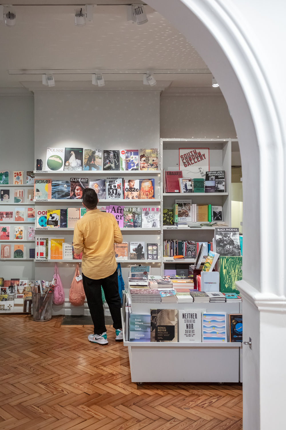 A person wearing a yellow shirt and black trousers looks at magazines displayed in an art gallery bookshop.