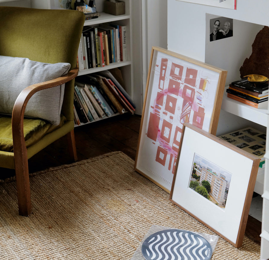 Framed artist prints sit beside a vinyl record on the ground in front of a bookshelf.