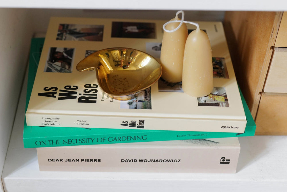 A pile of three books with a gold ashtray and two cream candles. 