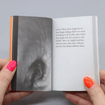 Inside pages of a book being held open by hands. On one page is a black and white photo of an eye.