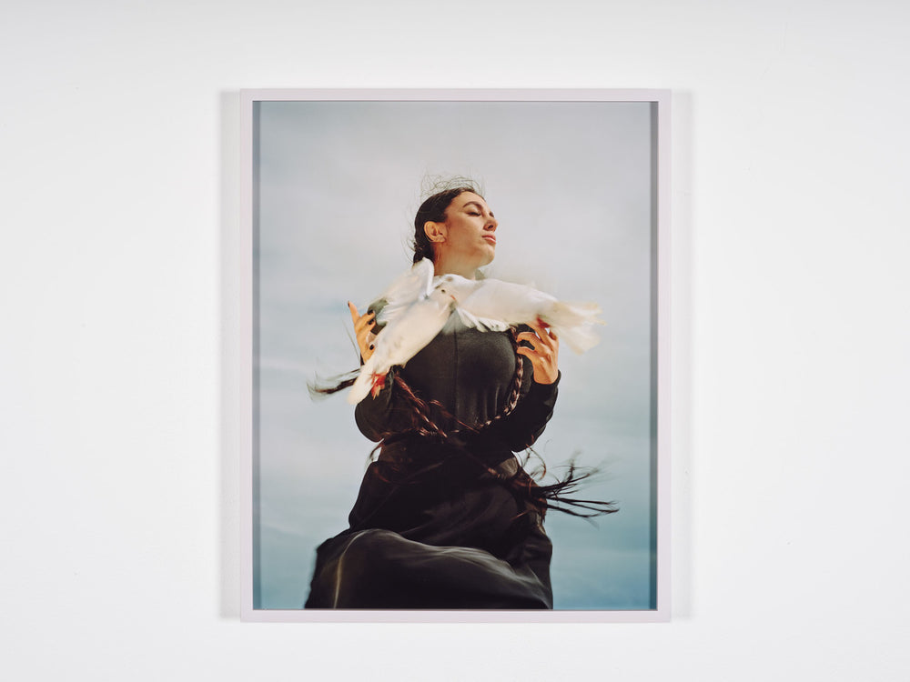 A photo by Hoda Afshar of a woman with long plaits holding a dove.