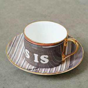 A grey tea cup and saucer with the word 'is' printed