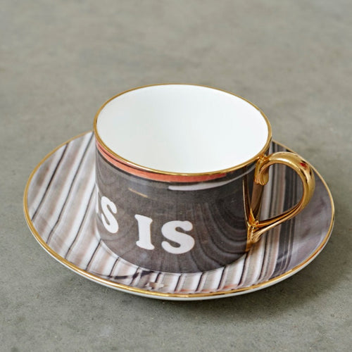 A grey tea cup and saucer with the word 'is' printed