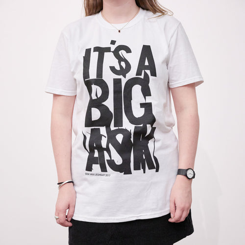 A person wearing a white t-shirt with black writing printed on it that reads It's a big ask. The t-shirt is a limited edition artwork.