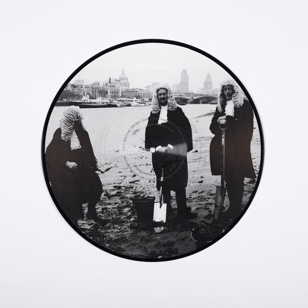 A black and white vinyl disk with a photograph of three people dressed as judges on the banks of the River Thames in London.