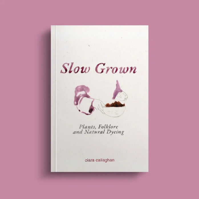 A book titled 'Slow Grown' by Ciara Callaghan on a pink background. There is this purple and brown watercolour painting design of hands holding a bowl.