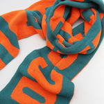 A bright orange and green football scarf with writing on it.