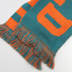 A bright orange and green football scarf with writing on it.