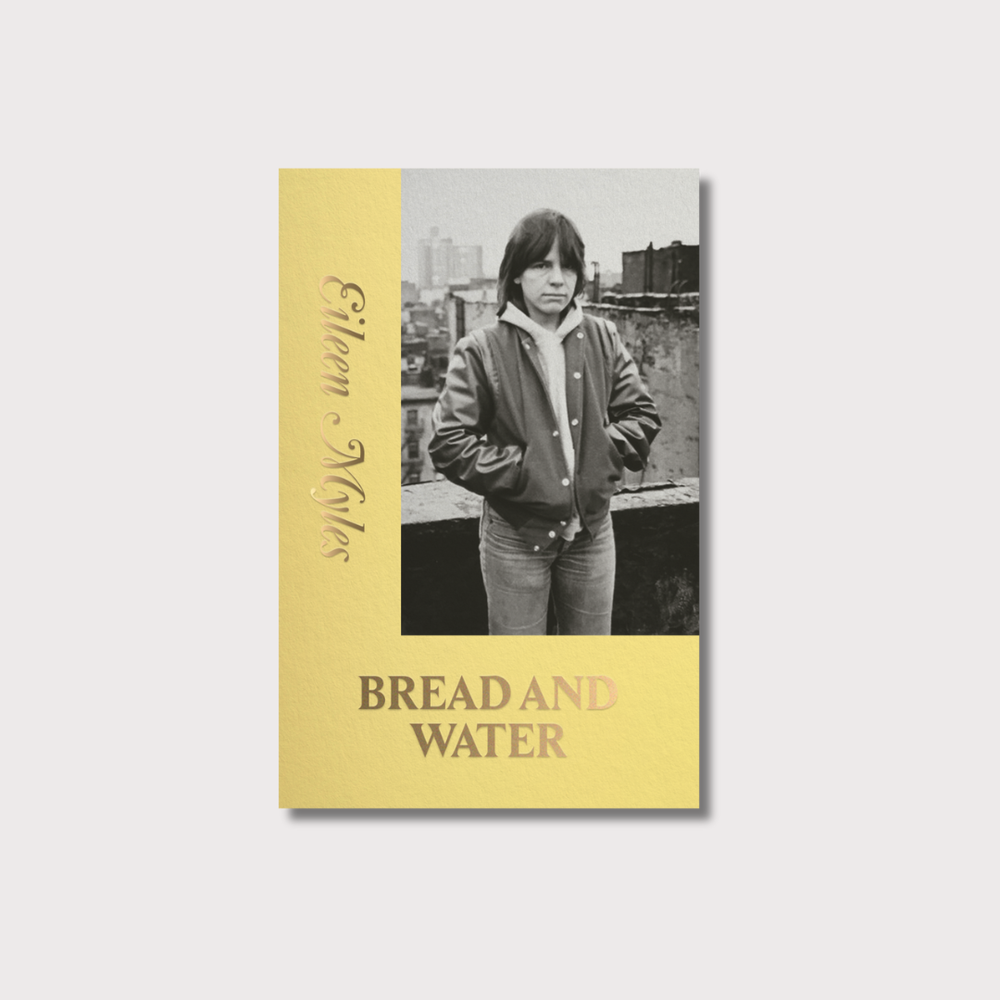 Yellow book cover shaped like an L with gold lettering for the author name, Eileen Myles vertically and the book title Bread and Water in capital letters horizontally. There is a black and white picture of the author standing against the New York City skyline in a bomber jacket, hoody and denim jeans. They are staring into the camera with a scowl and long brown hair