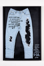 A limited edition artwork of ripped light blue jeans in a black frame. The jeans have black writing on them and the frame is signed in white ink in the bottom right corner.