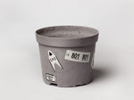 A grey plant pot with stickers on it by artist Magali Reus