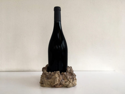 A black wine bottle set in stone on a beige background.