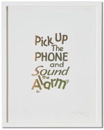 A framed print of a white page with metallic gold letters on it. This is a limited edition artwork by Rory Pilgrim. The text says Pick Up The Phone and Sound the alarm.