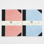Two notebooks on a grey background. The notebook on the left is red and white speckled with a black spine and black corners. The notebook on the right is blue and white speckled with a black spine and black corners.