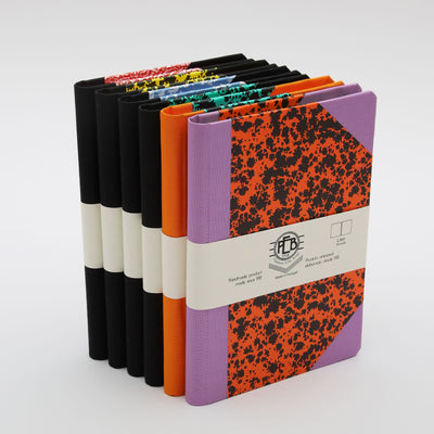 Six colourful stacked notebooks with orange, purple, and black spines.