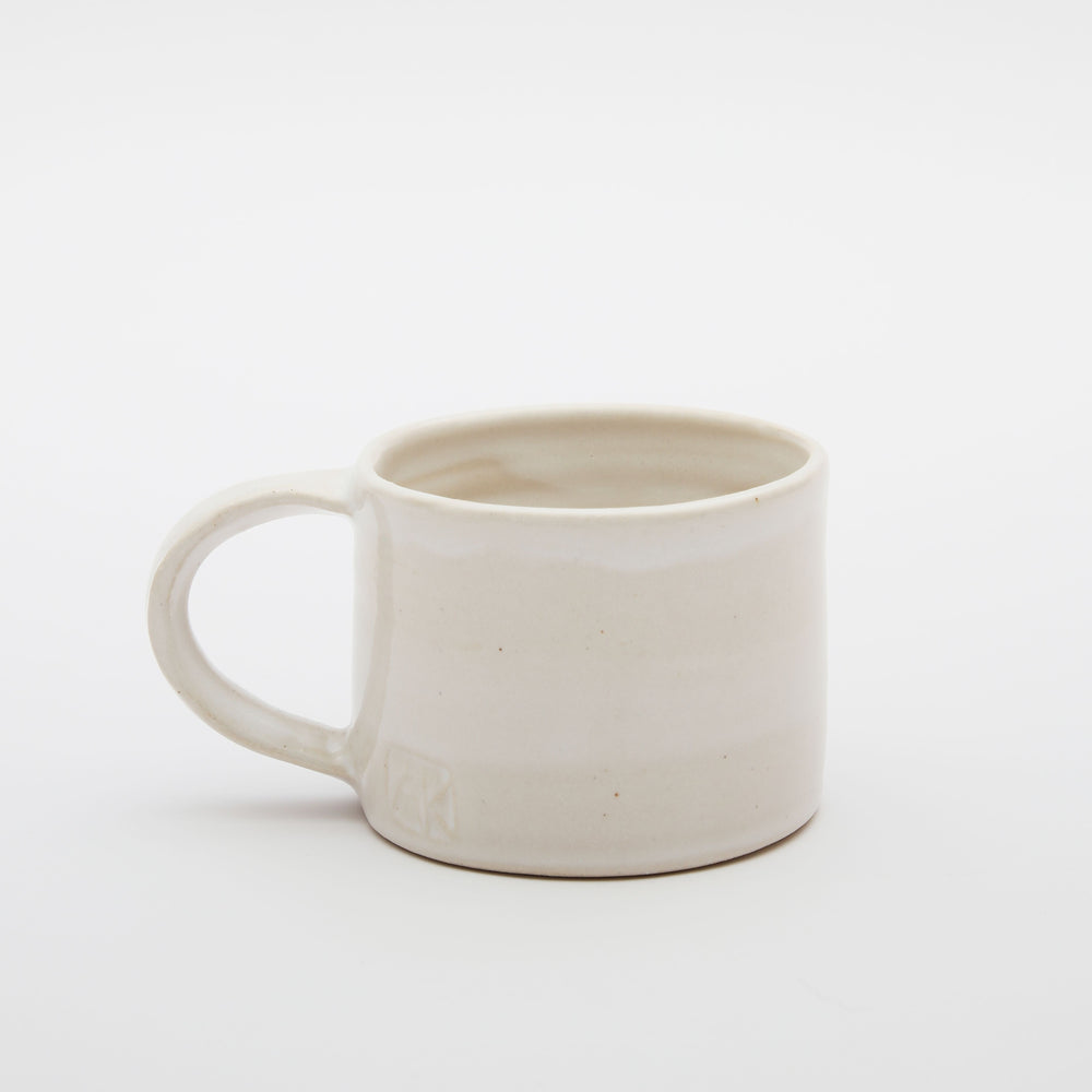 A white glazed ceramic mug with a handle. This cup was made in south London by artist Alice King
