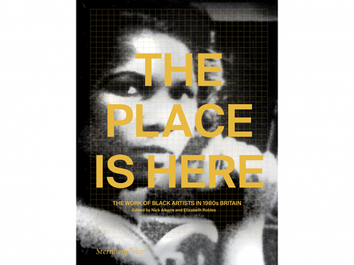 A book on  white background. The cover of the book has a black and white photo of a persons face and yellow text. The title of the book is 'The Place is Here: The work of Black Artists in 1980s Britain'. 