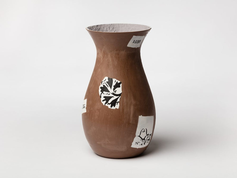 A brown vase with white stickers on it by artist Magali Reus